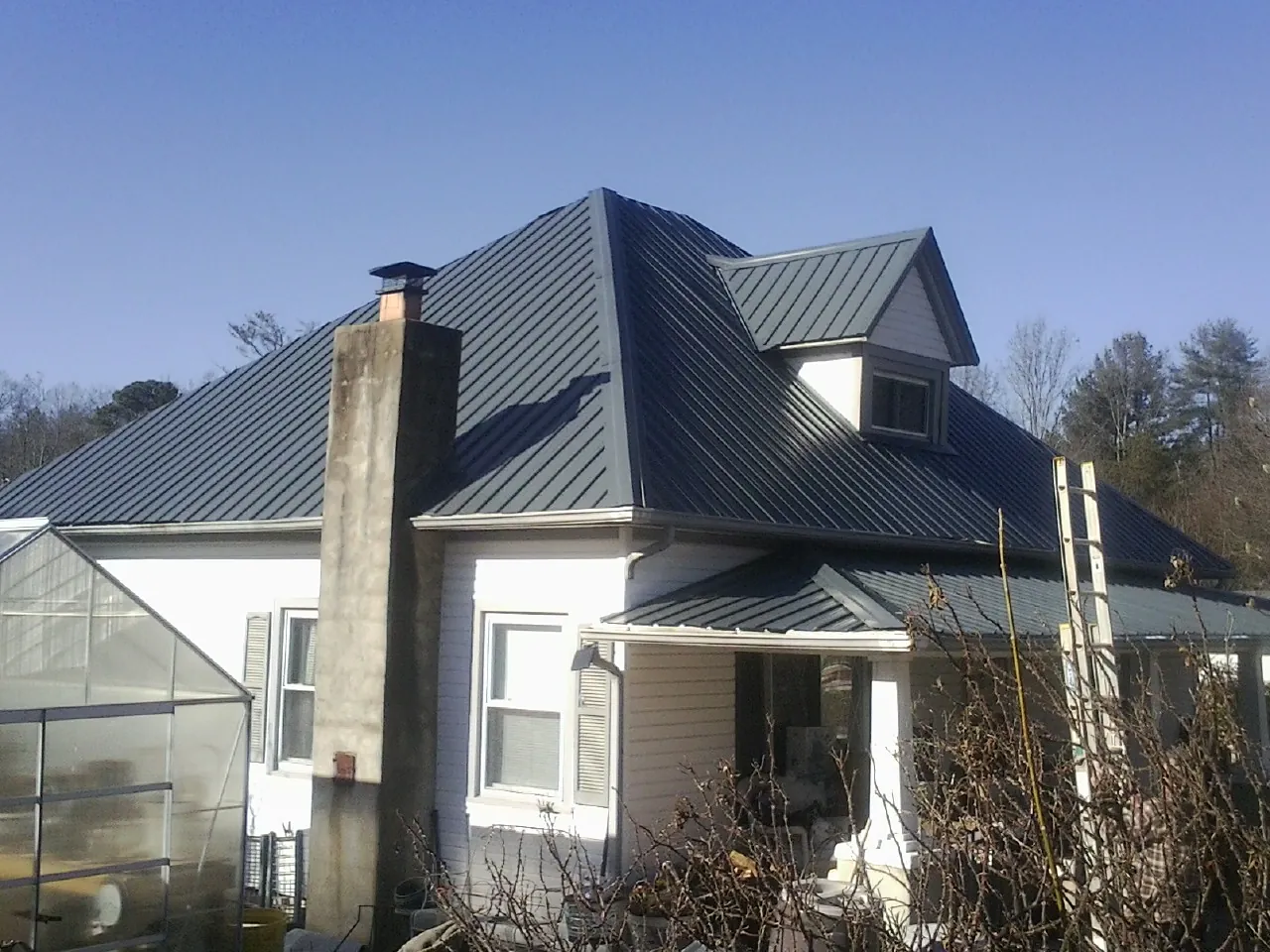 Dark blue standing seam metal roof on a white farmhouse with dormer — Slate & Tile Roof Repair by Roofing Brothers in Olanta