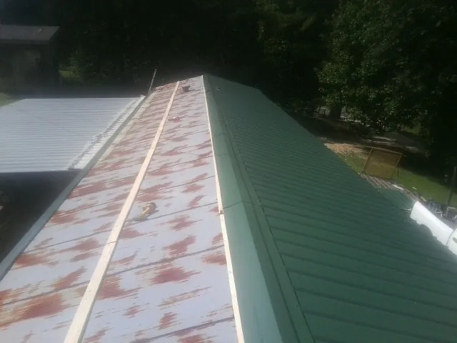 Old rusted panels beside newly installed green metal roofing — Wind Damage Roof Repair by Roofing Brothers in Olanta