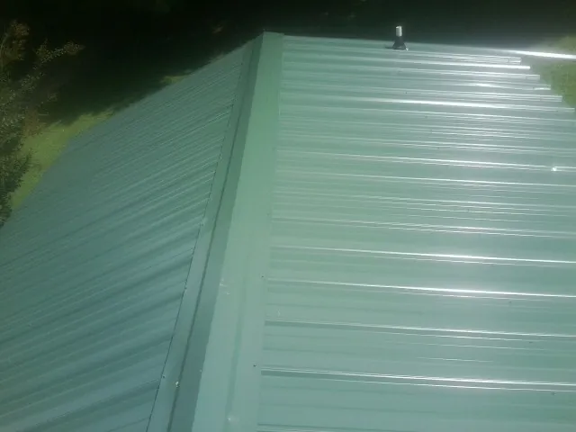New green metal panels meeting at the ridge of a roof — Flat Roof Repair work by our crew in Olanta