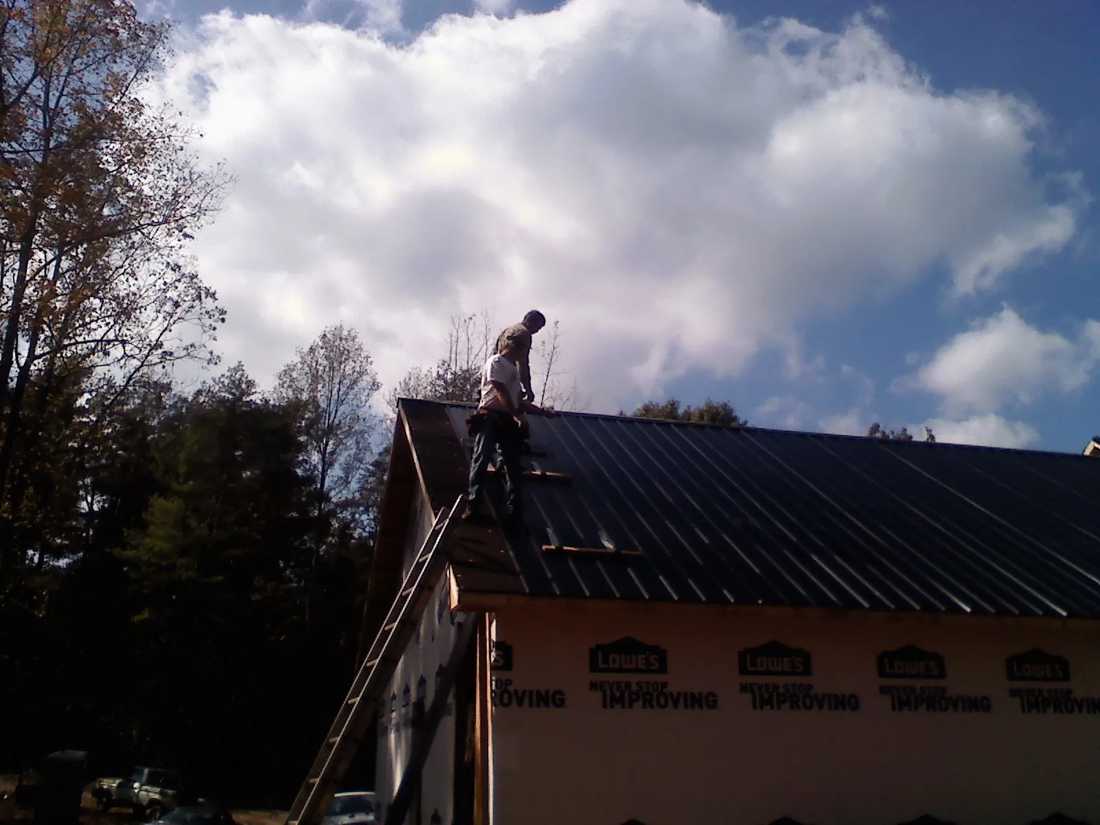 Roofer fastening dark metal panels high against a cloudy sky, from a Roof Inspection job in Olanta